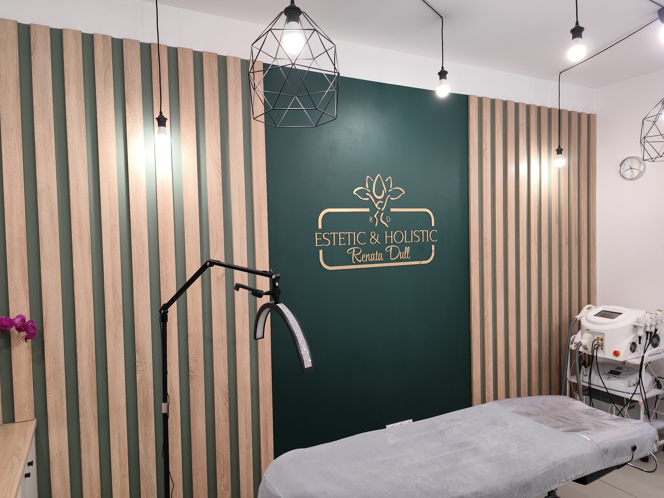Gabinet zabiegowy w RD ESTETIC and HOLISTIC, ściana w bottle green z gold logo Estetic and Holistic Renata Dull, drewniane listwy, czarne geometryczne lampy